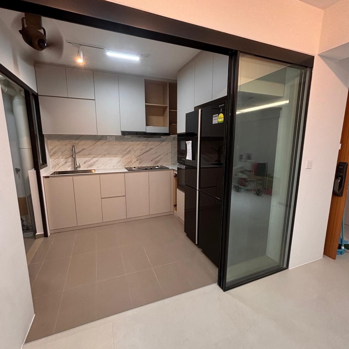 Bright white aluminium kitchen with black fridge behind a glass sliding door